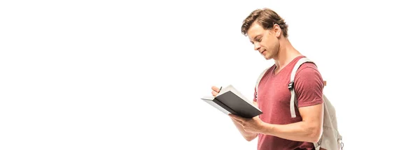 Panoramic shot of student with backpack writing on notebook isolated on white — Stock Photo