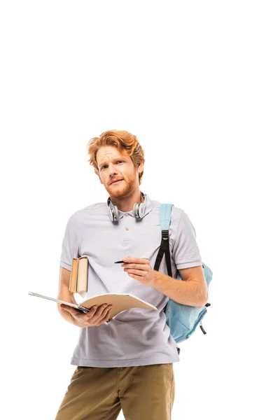 Student mit Rucksack hält Notizbuch und Stift in der Hand, während er die Kamera isoliert auf Weiß betrachtet — Stockfoto