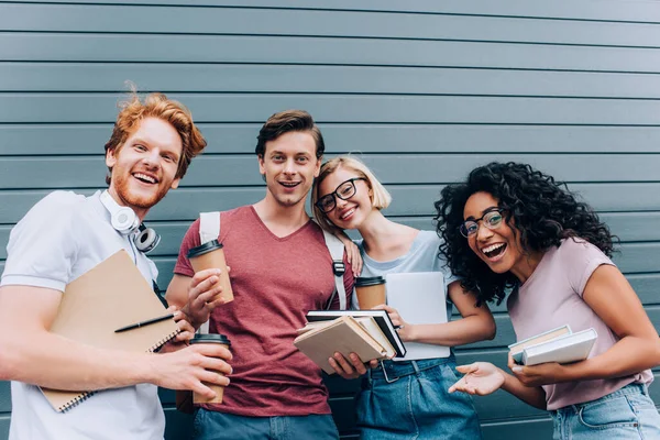 Studenti multietnici con caffè per andare e libri guardando la fotocamera sulla strada urbana — Foto stock