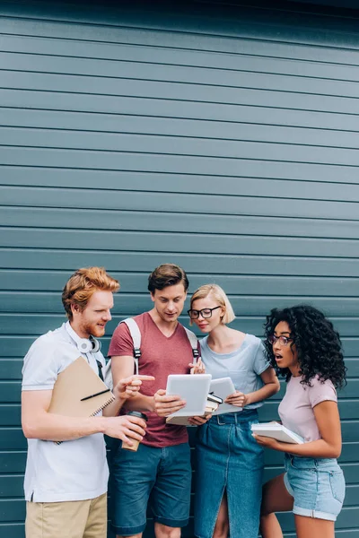 Multiethnic students pointing at digital tablet while standing on urban street — Stock Photo