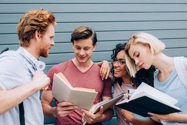 Étudiants multiethniques lisant des livres et tenant des cahiers dans la rue urbaine — Photo de stock