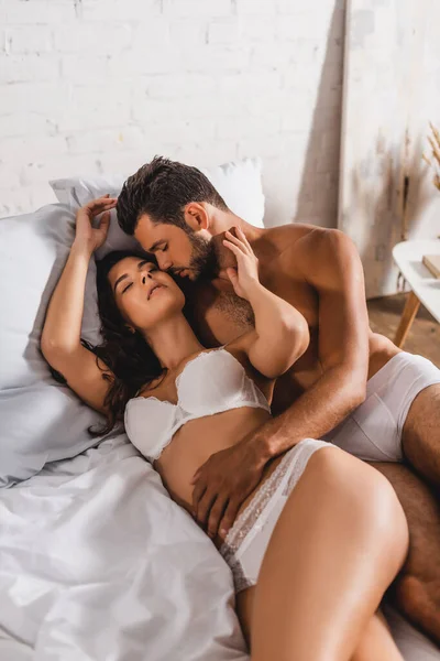 Shirtless man kissing and touching sensual girlfriend on bed — Stock Photo