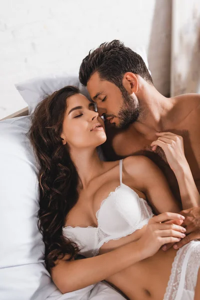 Musculoso hombre acostado cerca seductora novia con los ojos cerrados en la cama - foto de stock