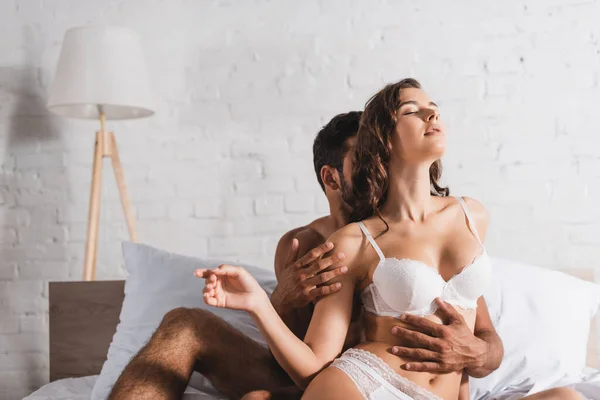 Мужчина без рубашки обнимает сексуальную женщину в нижнем белье на кровати — стоковое фото
