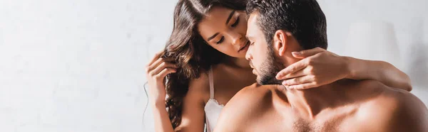 Cultivo horizontal de mujer seductora en sujetador abrazando al hombre musculoso en casa - foto de stock