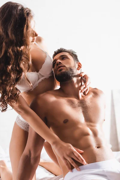 Selective focus of seductive woman touching torso of bearded boyfriend in underpants on bed — Stock Photo