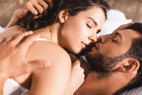 Selective focus of bearded man kissing girlfriend in bra on bed — Stock Photo