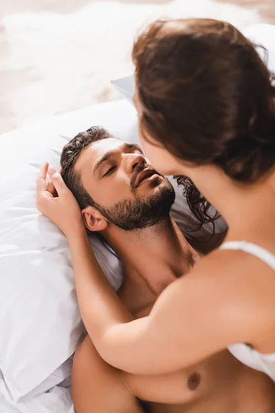 Selective focus of sexy woman in bra touching shirtless man on bed — Stock Photo