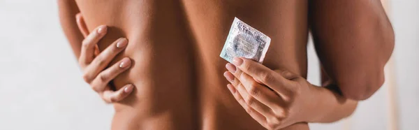 Plan panoramique de la femme touchant le dos de l'homme musclé et tenant le préservatif à la maison — Photo de stock