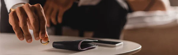 Cosecha panorámica del hombre poniendo anillo de bodas en la mesa de centro cerca de la cartera y el teléfono inteligente en el dormitorio - foto de stock