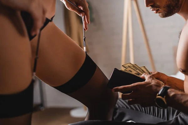 Selective focus of shirtless man holding dollars and wallet near sexy woman touching garter belt — Stock Photo