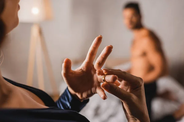 Selektiver Fokus einer Frau, die ihren Ehering ablegt, während sie neben einem Mann ohne Hemd im Schlafzimmer steht — Stockfoto