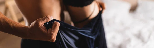 Horizontal crop of shirtless man holding dress of girlfriend in bedroom — Stock Photo