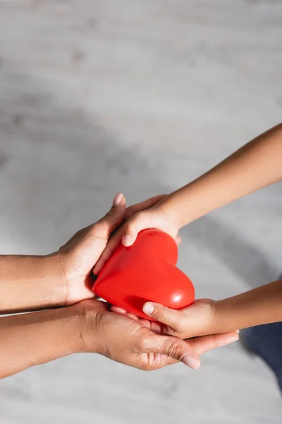 Vista de ángulo alto del modelo de corazón rojo en las manos ahuecadas de la madre y el niño afroamericanos - foto de stock