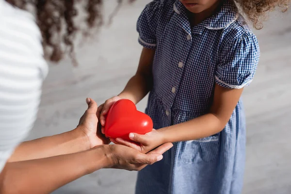 Cropped view of african american girl in dress holding heart model in cupped hands together with mother — Stock Photo