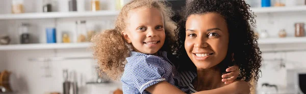 Imagen horizontal de la madre afroamericana sosteniendo a la hija en las manos y mirando a la cámara - foto de stock