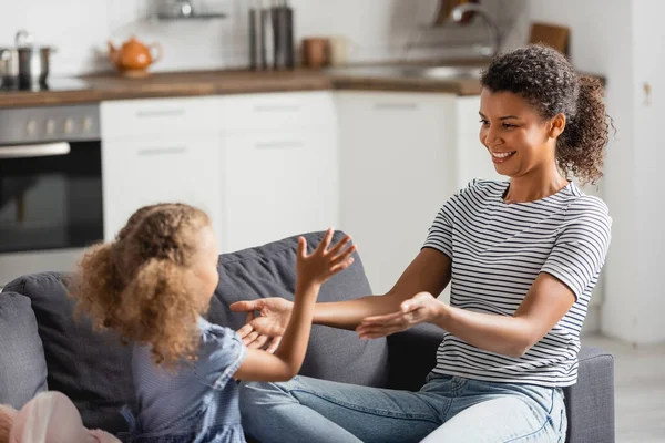 Jovem afro-americana em t-shirt listrada sentado com as mãos estendidas enquanto se diverte com a filha — Fotografia de Stock