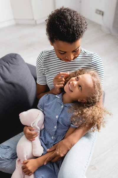 Vista ad alto angolo della donna afro-americana che si diverte con la figlia che tiene il coniglietto giocattolo — Foto stock