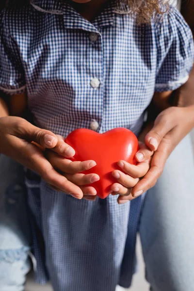 African american girl with mother holding heart model in cupped hands — Stock Photo