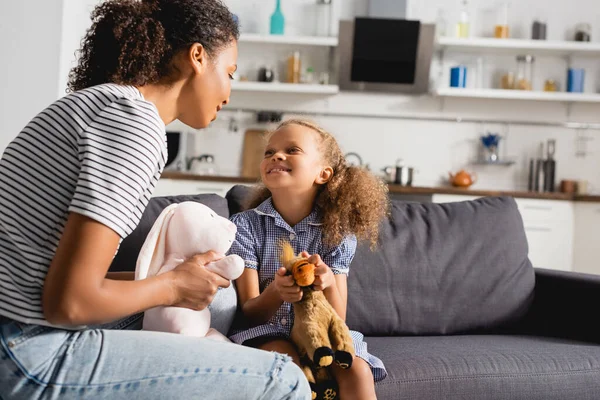 African american nanny and babysitter holding toys while looking at each other in kitchen — Stock Photo