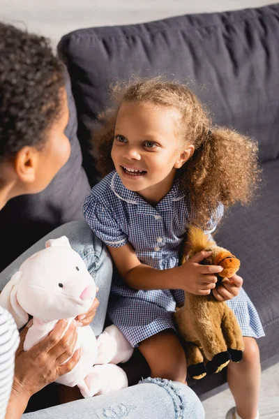 Visão de alto ângulo da menina americana africana com babá segurando brinquedos enquanto olham um para o outro — Fotografia de Stock