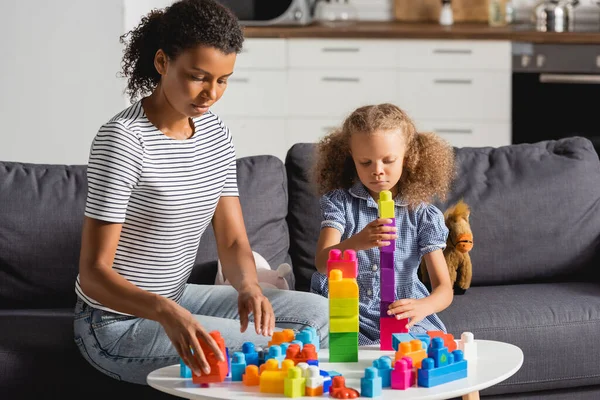 Jovem afro-americano babá e menina brincando com blocos de construção coloridos enquanto sentado no sofá — Fotografia de Stock