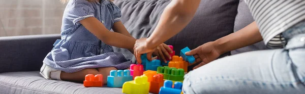 Abgeschnittene Ansicht eines afrikanisch-amerikanischen Babysitters und eines Kindes, das mit bunten Bausteinen auf dem Sofa spielt, horizontales Bild — Stockfoto