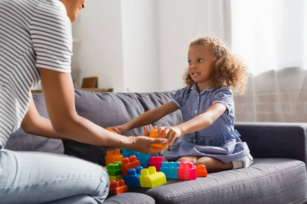 Partial view of nanny giving building blocks to african american girl while playing on sofa — Stock Photo