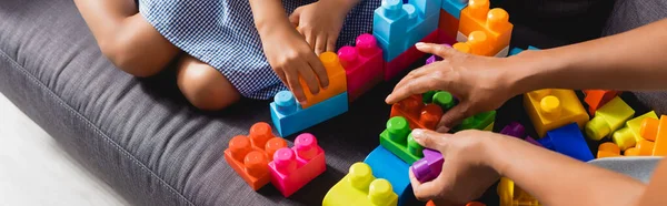 Vista cortada de afro-americano babá e menina brincando com blocos de construção multicoloridos, tiro panorâmico — Fotografia de Stock