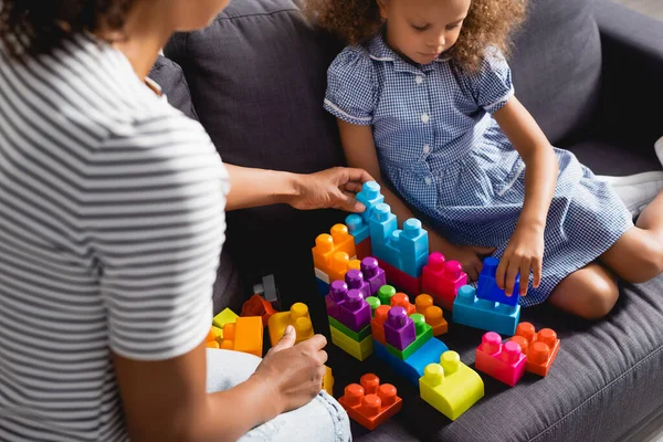 Vista ritagliata di babysitter vicino afro ragazza americana in abito da gioco con blocchi di costruzione multicolore — Foto stock