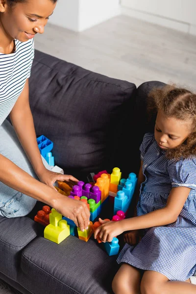 Vista ad alto angolo del bambino afro-americano con bambinaia che gioca con mattoni multicolori sul divano — Foto stock