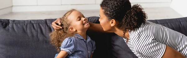 Panoramische Konzept der afrikanisch-amerikanischen Frau berührt Kopf der aufgeregten Tochter, während Spaß zu Hause — Stockfoto