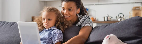 Panoramic crop of african american nanny behind girl using digital tablet on couch — Stock Photo