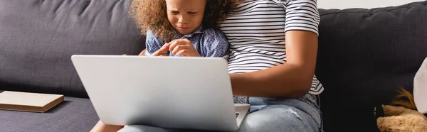 Cropped view of african american teleworker in striped t-shirt using laptop near upset daughter, horizontal image — Stock Photo