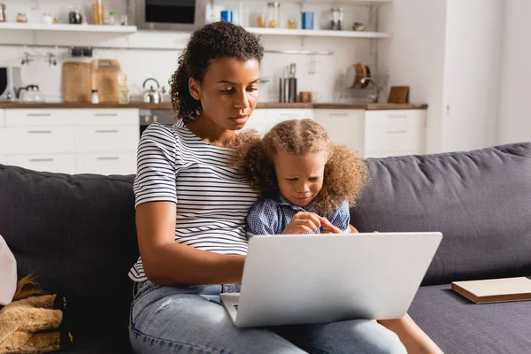 Afrikanisch-amerikanische Freelancer in gestreiftem T-Shirt mit Laptop in der Nähe verärgert Tochter in der Küche — Stockfoto