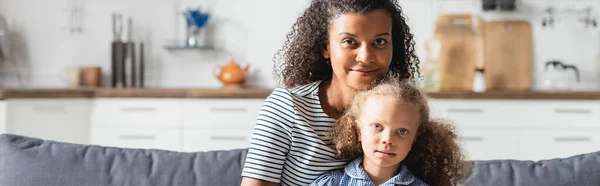 Cabeçalho do site da mãe americana africana com a filha olhando para a câmera enquanto sentado na cozinha — Fotografia de Stock