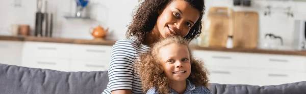 Panoramic shot of african american mom with child looking at camera in kitchen — Stock Photo