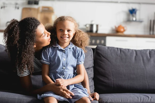 Young african american woman talking to daughter while sitting on sofa at home — Stock Photo
