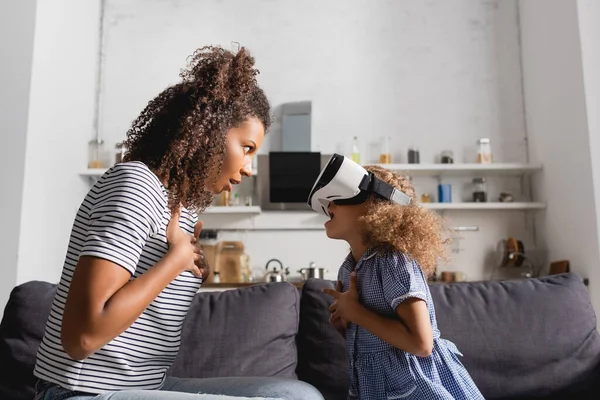 Excited african american babysitter and kid in vr headset looking at each other while holding hands on chests — Stock Photo