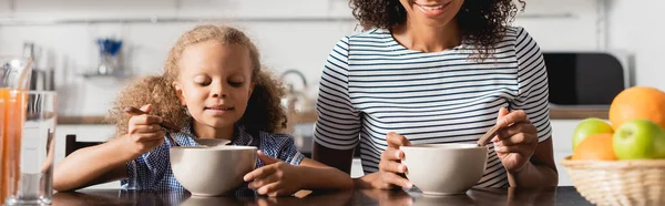 Vista recortada de mujer afroamericana en camiseta a rayas desayunando desde cuencos, plano panorámico - foto de stock