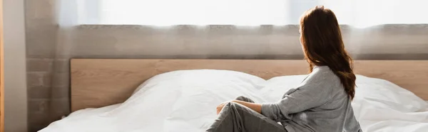 Горизонтальное изображение депрессивной брюнетки женщины, сидящей на кровати — стоковое фото