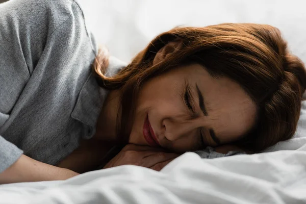 Mujer frustrada y morena con los ojos cerrados llorando en la cama - foto de stock