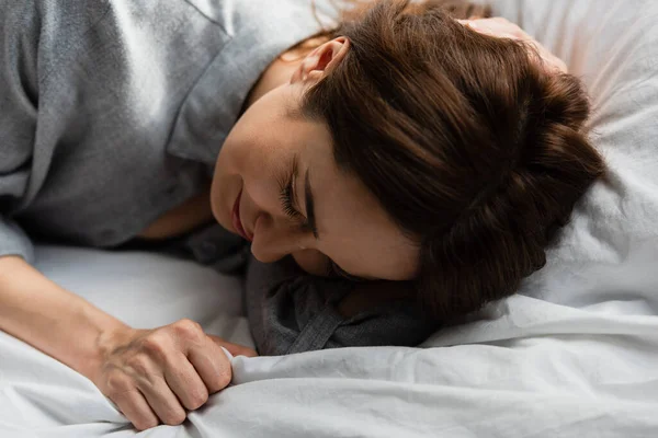 Selective focus of frustrated and brunette woman touching bedding while crying on bed — Stock Photo