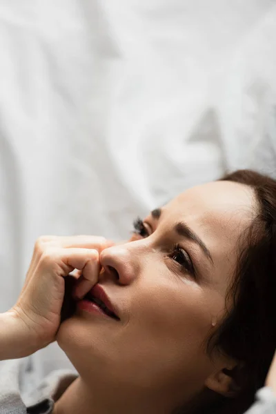 Frustrierte und brünette Frau berührt Gesicht, während sie auf dem Bett weint — Stockfoto