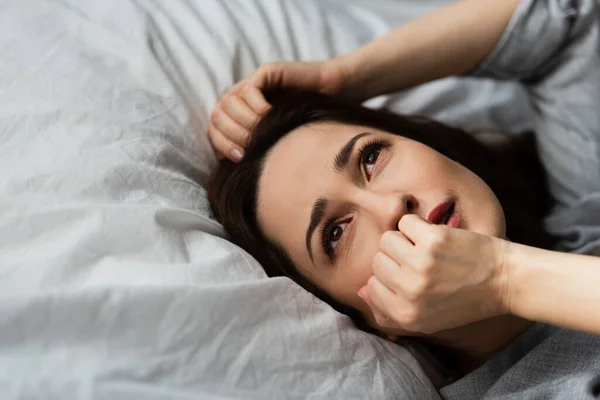 Розчарована і брюнетка жінка торкається обличчя, лежачи на ліжку — стокове фото