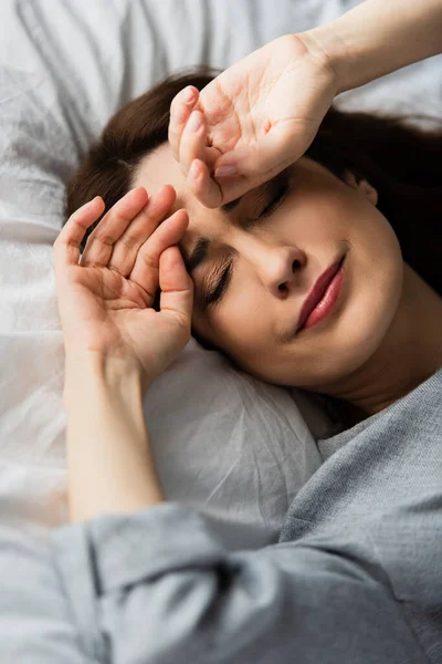 Вибірковий фокус сумна і брюнетка жінка торкається обличчя під час плачу на ліжку — стокове фото