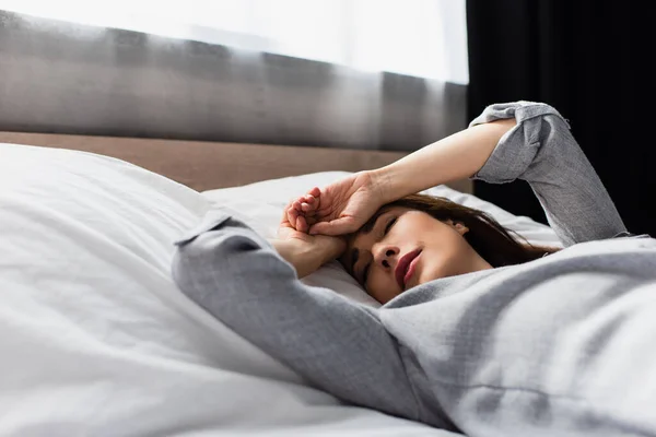 Mujer triste y morena tocando la cara mientras está acostado en la cama - foto de stock