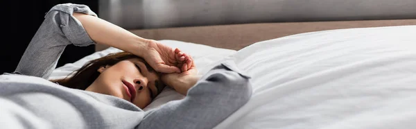 Горизонтальный урожай грустной и брюнетки женщины касающейся лица, лежащей на кровати — стоковое фото