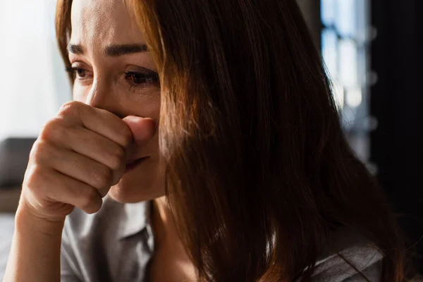 Крупним планом засмучена і брюнетка жінка торкається обличчя під час плачу вдома — стокове фото