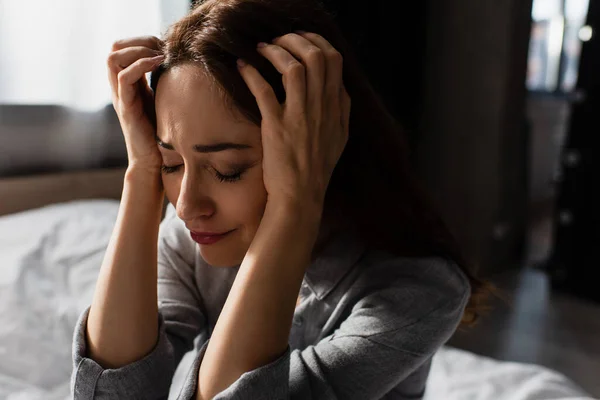 Aufgebracht und brünette Frau berührt Haare, während sie zu Hause weint — Stockfoto